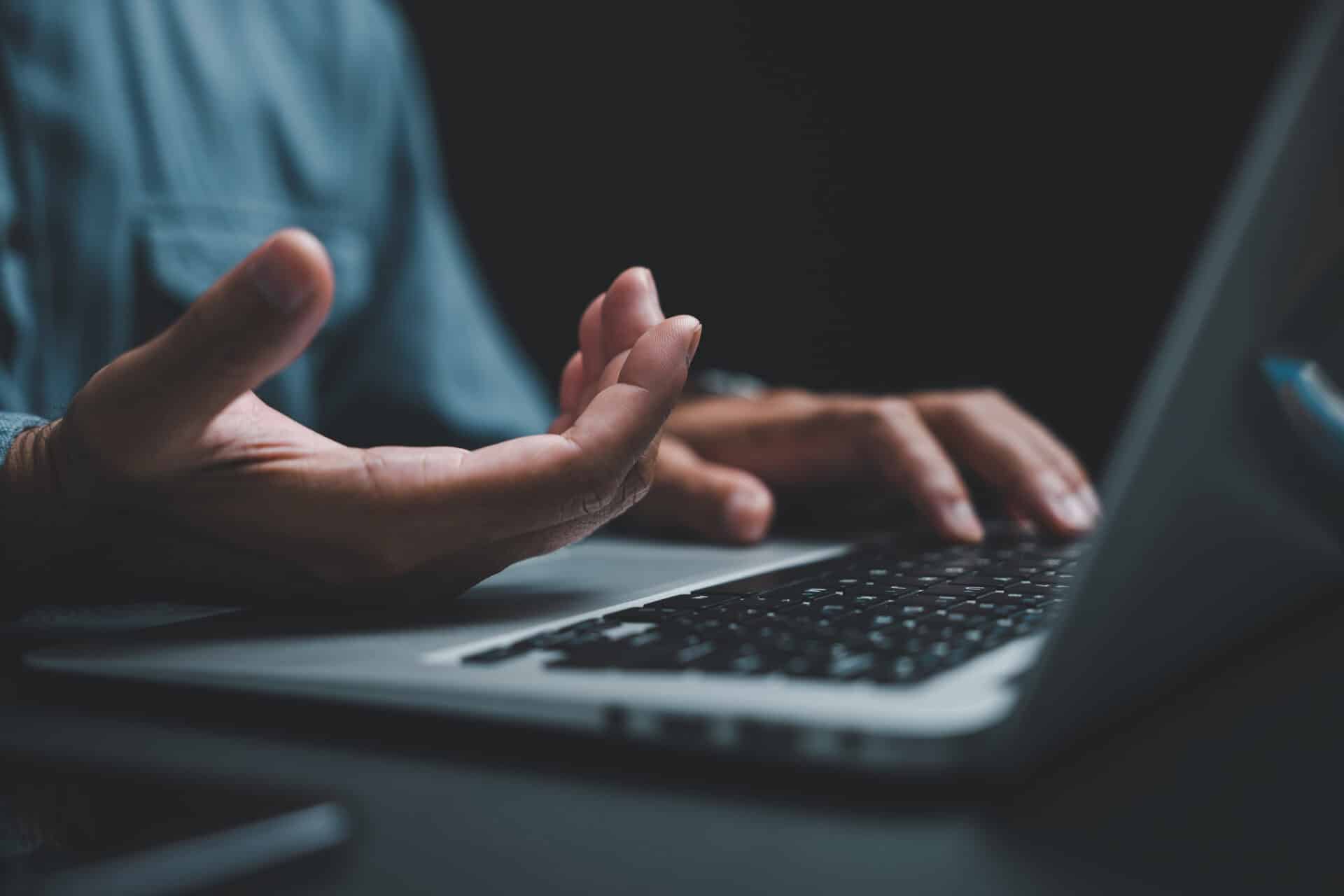 close up of hand gesturing over laptop keyboard, dark background.