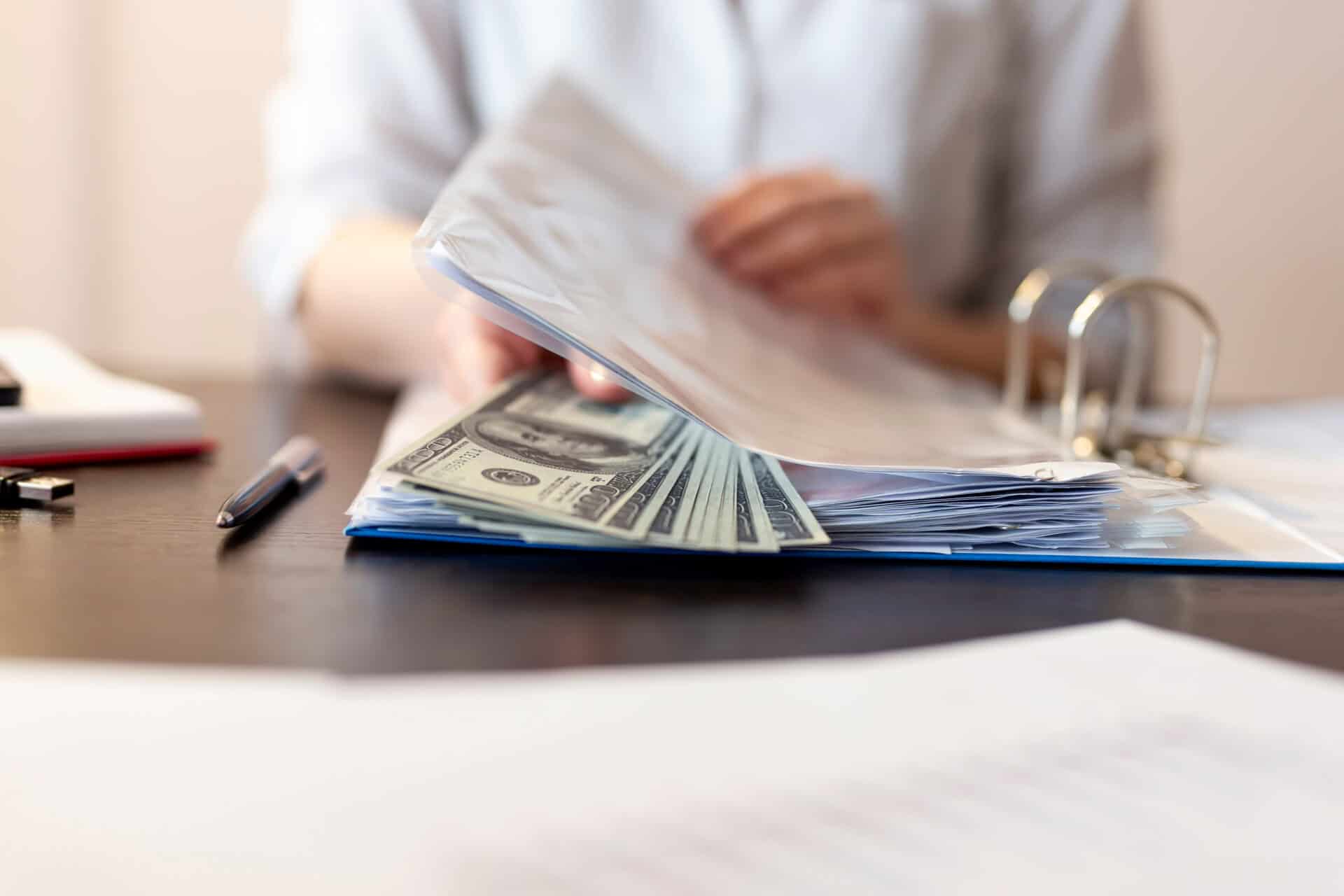 Detail of businesswoman's hands receiving bribe money in file while reviewing the contracts. Selective focus on the money