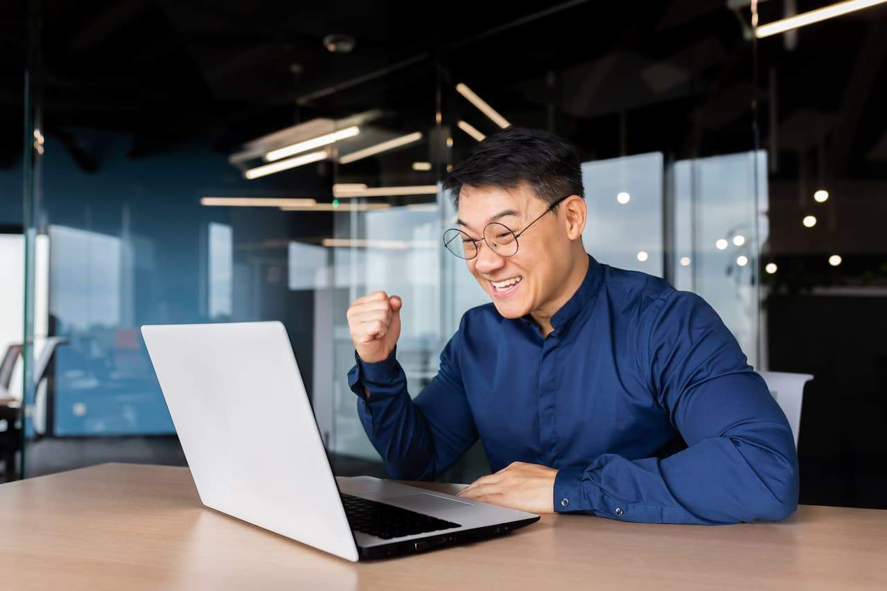 A happy Asian man sits in the office with laptop